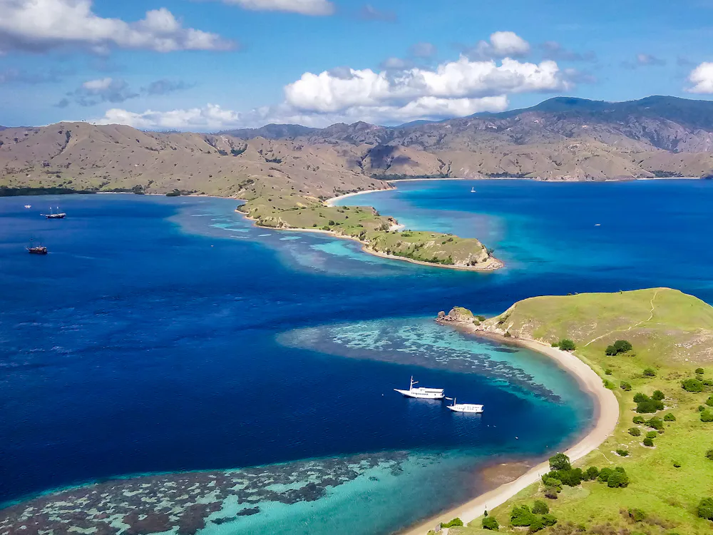 Aerial view of a reef-fringed tropical island with boats at anchor