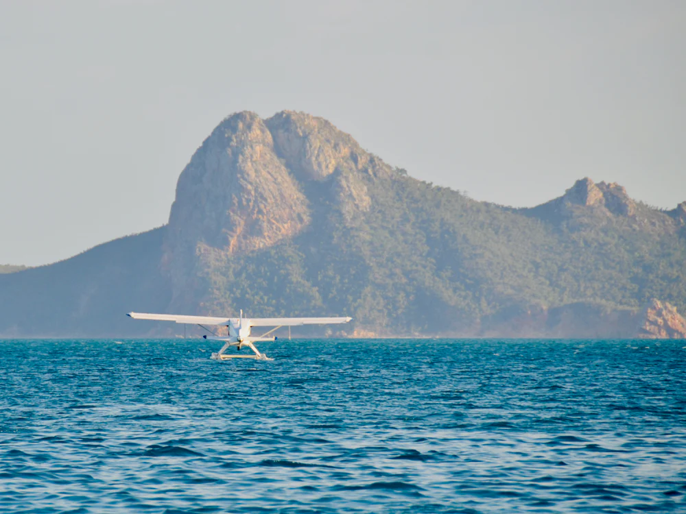 A small floatplane on the water below a coastal ridge