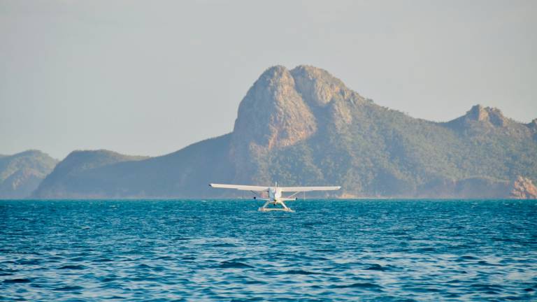 A small floatplane on the water below a coastal ridge