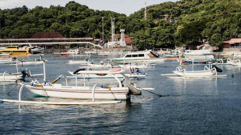 Wooden outrigger boats moored along a busy Indonesian harbour
